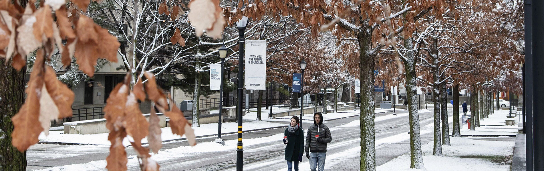 Two students walk with coffees on snowy St. George Street